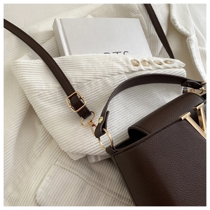 Detail of dark brown lychee leather texture and golden metal V buckle on crossbody bag