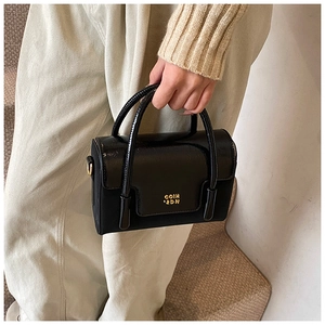 Detail of black glossy patent leather handbag with gold metallic logo and hardware
