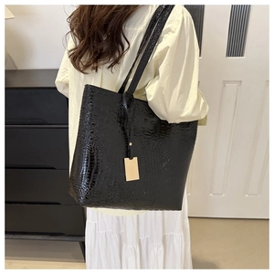Détail d'un sac cabas noir en cuir croco avec élégante étiquette métallique dorée
