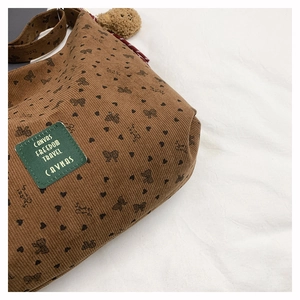 Détail d'un sac cabas en velours marron avec motifs cœurs et un pendentif ours peluche