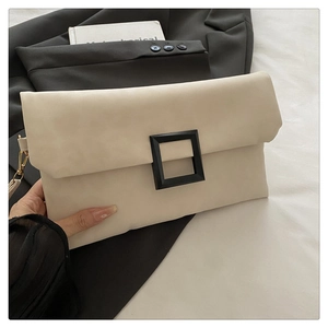 Detail of a beige leather envelope clutch with a matte black buckle on a white bed