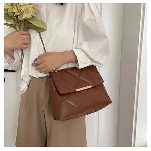 Detail of dark brown quilted crossbody bag with gold hardware and chain strap on model