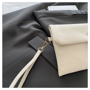 Detail of minimalist beige envelope clutch bag with gold hardware on gray blazer background
