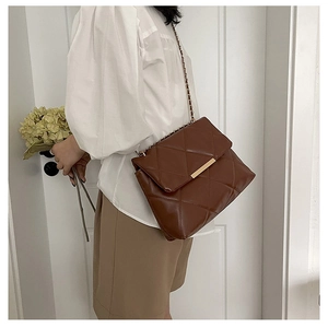 Detail of dark brown quilted crossbody bag with golden hardware and chain strap