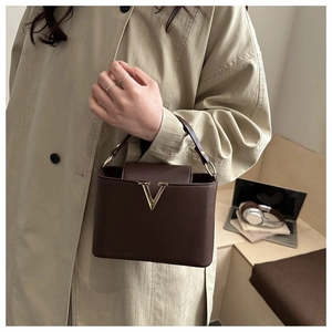 Close-up of minimalist dark brown litchi grain handbag with a gold V-shaped metal clasp