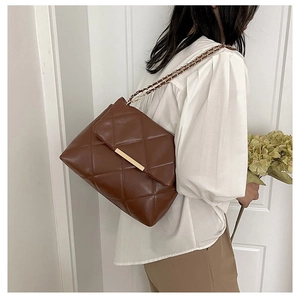 Detail of brown quilted leather bag featuring a glossy finish and gold metal bar buckle