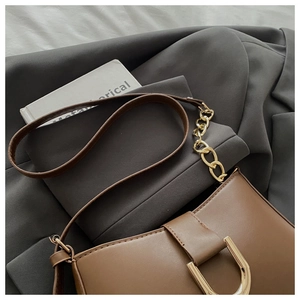 Détail du sac en cuir marron avec boucle en D dorée et bandoulière chaîne sur un costume