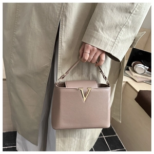 Detail of greyish pink lychee grain leather handbag with gold V-shaped metal clasp