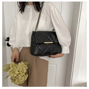 Close-up of black quilted leather chain bag worn by a model in a minimalist setting