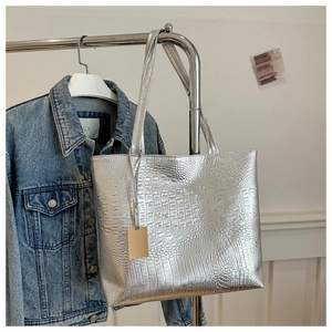Sac fourre-tout argenté à motif crocodile sur un cintre devant une veste en jean