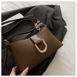 Détail du sac baguette marron avec boucle fer à cheval dorée et bandoulière chaîne sur veste