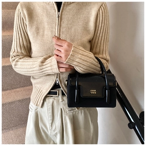 Close-up of black glossy PU leather handbag with gold COIH 2DN text and short handle