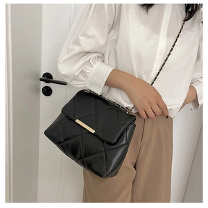 Detail of black quilted crossbody bag with gold metal trim and chain strap on a model