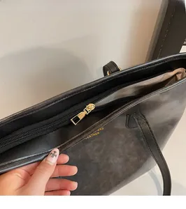 Close-up of golden zipper detail and embossed gold lettering on black leather tote bag