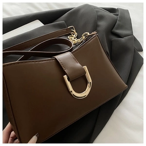 Détail d'un sac à bandoulière marron avec boucle fer à cheval dorée et bandoulière chaîne