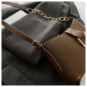 Détail d'un sac baguette en cuir café avec chaîne dorée sur une veste de blazer