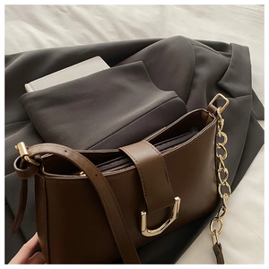 Détail du sac baguette marron foncé avec boucle dorée en D et bandoulière chaîne