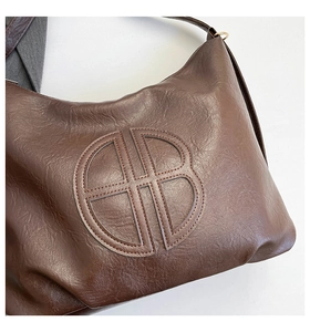 Dettaglio borsa tote in morbida pelle marrone scuro con logo circolare e grana naturale