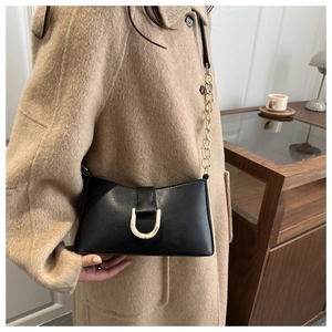 Détail d'un sac porté épaule en cuir noir avec boucle fer à cheval dorée et chaîne