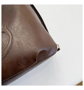 Dettaglio della borsa tote in pelle marrone scuro con cuciture e fibbie metalliche