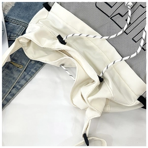 Detail of white drawstring tote bag with black mesh stitching and large letter print