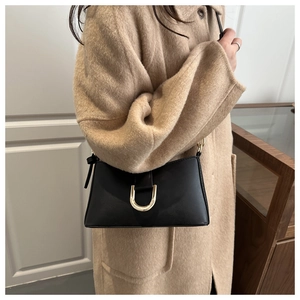 Détail d'un sac sous les bras noir avec boucle en U dorée sur un manteau en laine marron