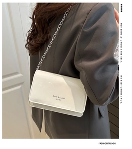 Detail view of white patent leather crossbody bag with silver chain strap and brand lettering