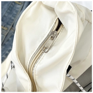 Detail of white nylon tote bag showing metallic zipper and textured drawstring closure