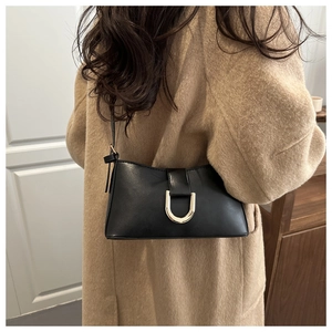 Détail du sac bandoulière noir élégant avec boucle dorée en U sur un manteau beige