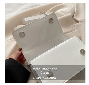 Close-up of dual silver magnetic buckles and white patent leather finish on handbag