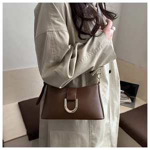Détail d'un sac bandoulière marron avec boucle fer à cheval dorée et lanière en chaîne