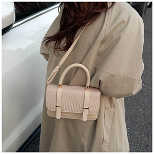 Detail of beige textured woven flap handbag with gold buckle and adjustable strap