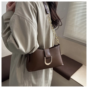 Détail du sac en cuir marron avec boucle en D dorée porté avec un trench-coat