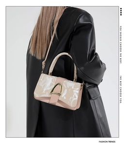 Detail of elegant beige crossbody bag with gold buckle on a black leather jacket