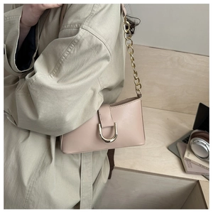 Détail de la boucle dorée en D et de la chaîne métallique sur un sac baguette beige