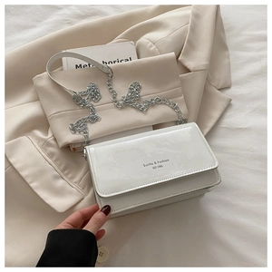 Close-up of white patent leather shoulder bag with silver chain strap on beige blazer