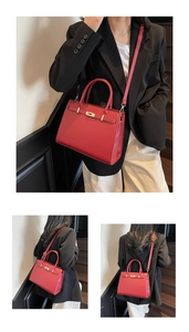 Detail of red leather Kelly style handbag showing golden twist lock and textured finish