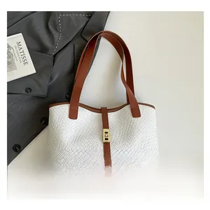 Detail of white crocodile textured tote bag with brown leather trim and golden clasp