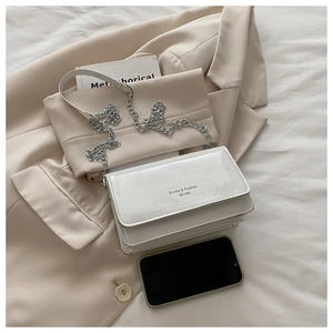 Top view of a white patent leather crossbody bag with silver chain on a beige blazer