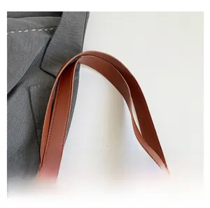 Detail shot of brown leather handle with neat stitching on white faux croc tote bag
