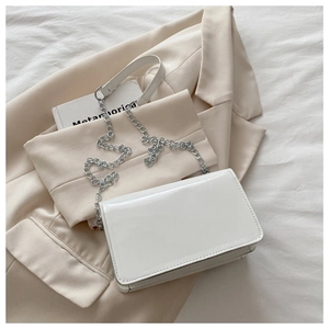 Close-up of a white patent leather shoulder bag with a silver chain on a beige blazer