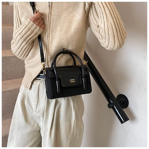Close-up of a stylish black glossy handbag with golden lettering and metal buckles