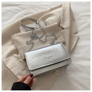 Detail of silver metallic textured crossbody bag with chain strap on beige blazer