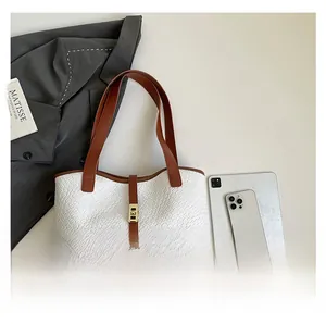 Flat lay of large tote bag with woven texture, leather straps, and office accessories