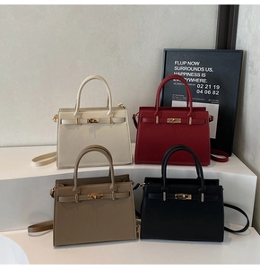 Four textured Kelly bags in white, red, brown, and black on a minimalist display