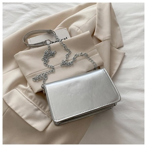 Detail of silver chain strap on glossy metallic crossbody bag over beige blazer