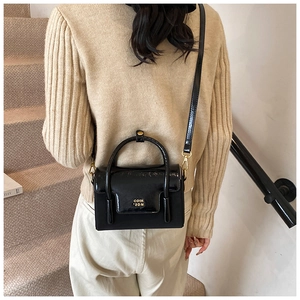 Detail of black patent leather crossbody bag with gold hardware and logo on beige stairs
