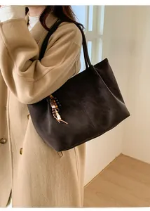 Dettaglio della borsa tote in pelle scamosciata marrone con pendente etnico e ampia capienza