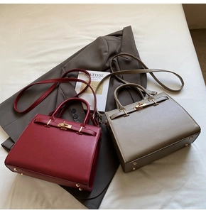 Detail of burgundy and khaki textured leather handbags with metal turn-lock and protective feet