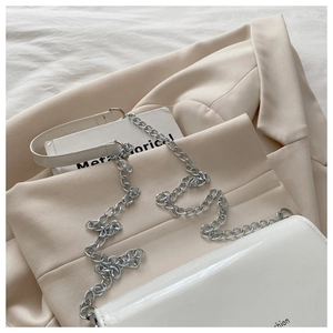 Close-up of white glossy crossbody bag with silver chain strap on beige blazer